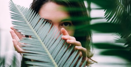Mulher jovem com cara escondida por folha de palmeira